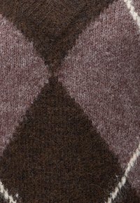 Gros plan d’un tissu en laine doux et texturé avec un motif à losanges argyle couleur marron foncé et mauve atténué.
