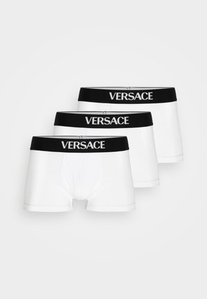 Trois paires de boxers blancs avec des ceintures élastiques noires comportant le logo "VERSACE" en lettres blanches. Texture de tissu lisse.