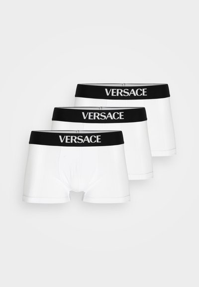 Three pairs of white boxer shorts with black elastic waistbands featuring the "VERSACE" logo in white lettering. Smooth fabric texture.