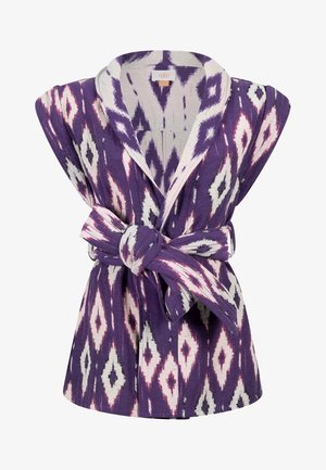 Ärmellose lila Jacke mit weißem und pinkfarbenem Rautenmuster, weitem Reverskragen und Stoffgürtel, der in der Taille zu einer Schleife gebunden ist.