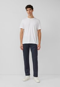 Weißes Baumwoll-T-Shirt mit kurzen Ärmeln, kombiniert mit marineblauen Hosen und weißen Turnschuhen. Das Outfit hat ein lässiges, minimalistisches Design.