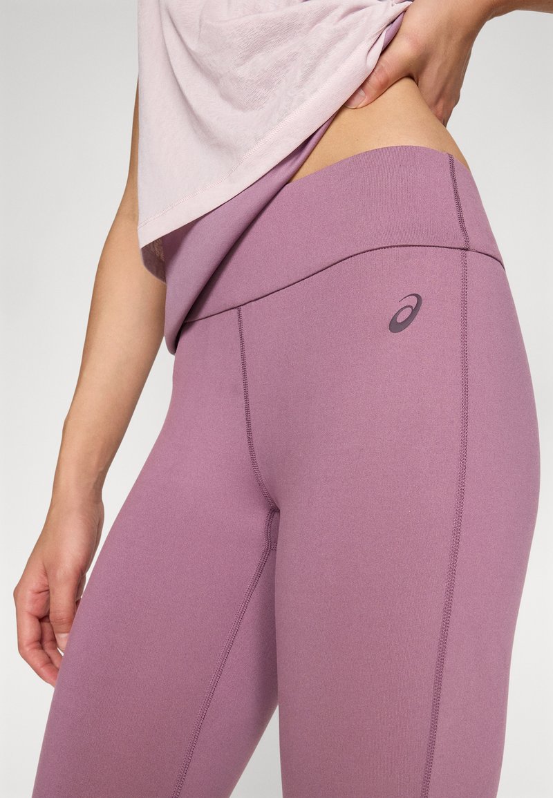 Les leggings taille haute lilas présentent une texture lisse, des coutures plates et un petit logo près de la taille, mettant en valeur une silhouette ajustée.