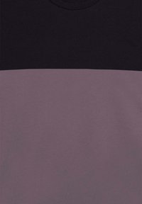 Camiseta de algodón con cuello redondo; presenta una mitad superior negra y una mitad inferior malva con una textura suave y costuras limpias.