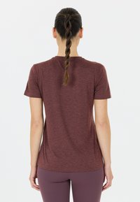 Mörkröd t-shirt med kort ärm, en slät textur, rund halslinning och en lätt kurva vid nederkanten, ihop med matchande leggings.