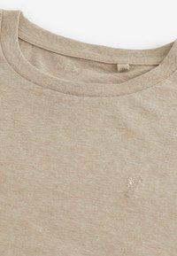 T-shirt beige à col rond avec une texture en maille fine et un petit logo brodé de tête de cerf sur le côté gauche de la poitrine.