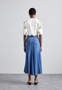 Haut blanc à manches bouffantes avec des détails en dentelle, associé à une jupe en jean taille haute. La jupe a une forme évasée et des poches arrière. Sandales à talons noirs.