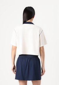 Vit kortärmad polo med marinblå krage och detaljer, parat med en marinblå kjol med elastisk midja. Mjuk textur med en avslappnad passform.
