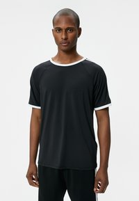 Zwarte t-shirt met korte mouwen en witte rand bij de halslijn en mouwen, gemaakt van gladde stof, met een ontspannen pasvorm en raglanmouwen.