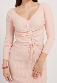 Rosa geripptes Langarmoberteil mit tiefem V-Ausschnitt und gerafftem Frontdetail, ausgestattet mit einem Kordelzug in der Taille für eine anpassbare Passform.