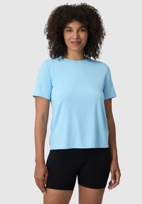 Světle modré tričko s krátk�ým rukávem a kulatým výstřihem, vyrobené z hladkého materiálu, v kombinaci s černými těsnými šortkami.