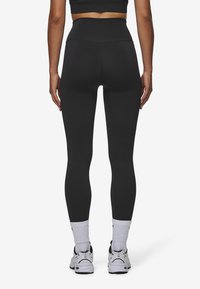 Zwarte high-waisted leggings van rekbaar materiaal, met een gladde textuur en een strakke pasvorm. Draagt witte sokken en sneakers.