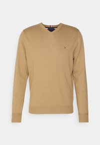 Kamelinvärinen V-aukollinen pitkähihaisen neulepuseron vasemmassa rinnassa on pieni Tommy Hilfiger -logo, resoroidut hihansuut ja helma.