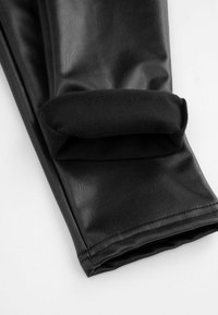 Czarne legginsy z sztucznej skóry z miękkim czarnym polarem w okolicy kostek, charakteryzujące się gładką fakturą i starannym przeszyciem.