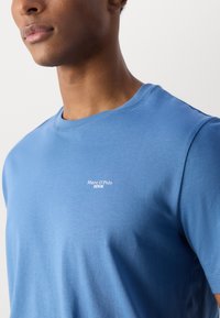 Blauwe ronde hals t-shirt van zacht stof, met een klein wit "Marc O'Polo DENIM" logo op de borst. Eenvoudige, aansluitende pasvorm.
