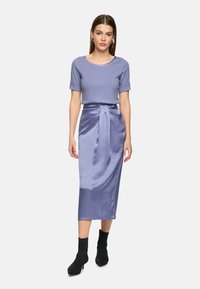 Light purple top with short sleeves paired with a satin light purple midi skirt, tied at the waist, worn with black ankle boots.