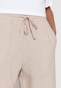 Beiga, lätta byxor i bomullsblandning med elastisk midja, snörning och sidofickor. Texturen verkar mjuk och avslappnad.