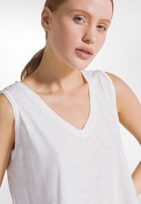 Top blanco sin mangas con diseño de escote en V, fabricado con tela ligera, que presenta una superficie ligeramente texturizada y una caída suave.