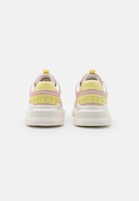 Un paio di sneaker pastello rosa e giallo con spesse suole bianche, testo del marchio Marc O'Polo sulla cinghia gialla e nell'area del tallone, rivolte all'indietro.