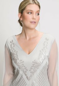 Top grigio chiaro con scollatura a V, maniche lunghe trasparenti e intricati ricami argentati con motivi a foglia e dettagli di perline.