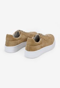 Zapatillas de ante beige con suela de goma blanca, que presentan un diseño de cordones, detalles perforados y un forro interior suave.