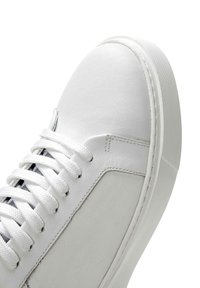 Sneaker blanche avec une tige en cuir lisse, bout rond et lacets plats. Semelle en caoutchouc texturée avec un design minimaliste et de subtiles détails de couture.