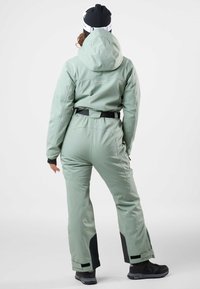 Mint green waterproof ski suit with a fitted silhouette, adjustable hood, and black accents at cuffs and ankles. Durable fabric with a belt.