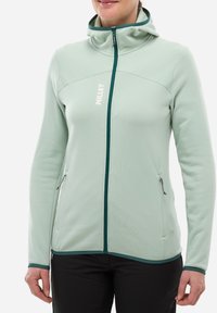 Veste softshell vert menthe avec fermeture éclair, col montant, poches latérales et accents contrastants vert foncé le long de la fermeture éclair et de l'ourlet.