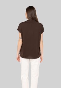 Haut marron à manches courtes avec une coupe décontractée. Texture lisse et ourlet arrondi, porté avec un pantalon blanc. Design simple avec un col discret.