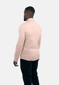 Helles rosa Langarm-Polohemd aus glattem Stoff, mit klassischem Kragen, schmaler Passform und abgerundetem Saum. Getragen mit dunklen Hosen.