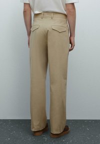 Beige wide-leg trousers made from smooth fabric, featuring a mid-rise waist, two back pockets, and a clean, streamlined silhouette.