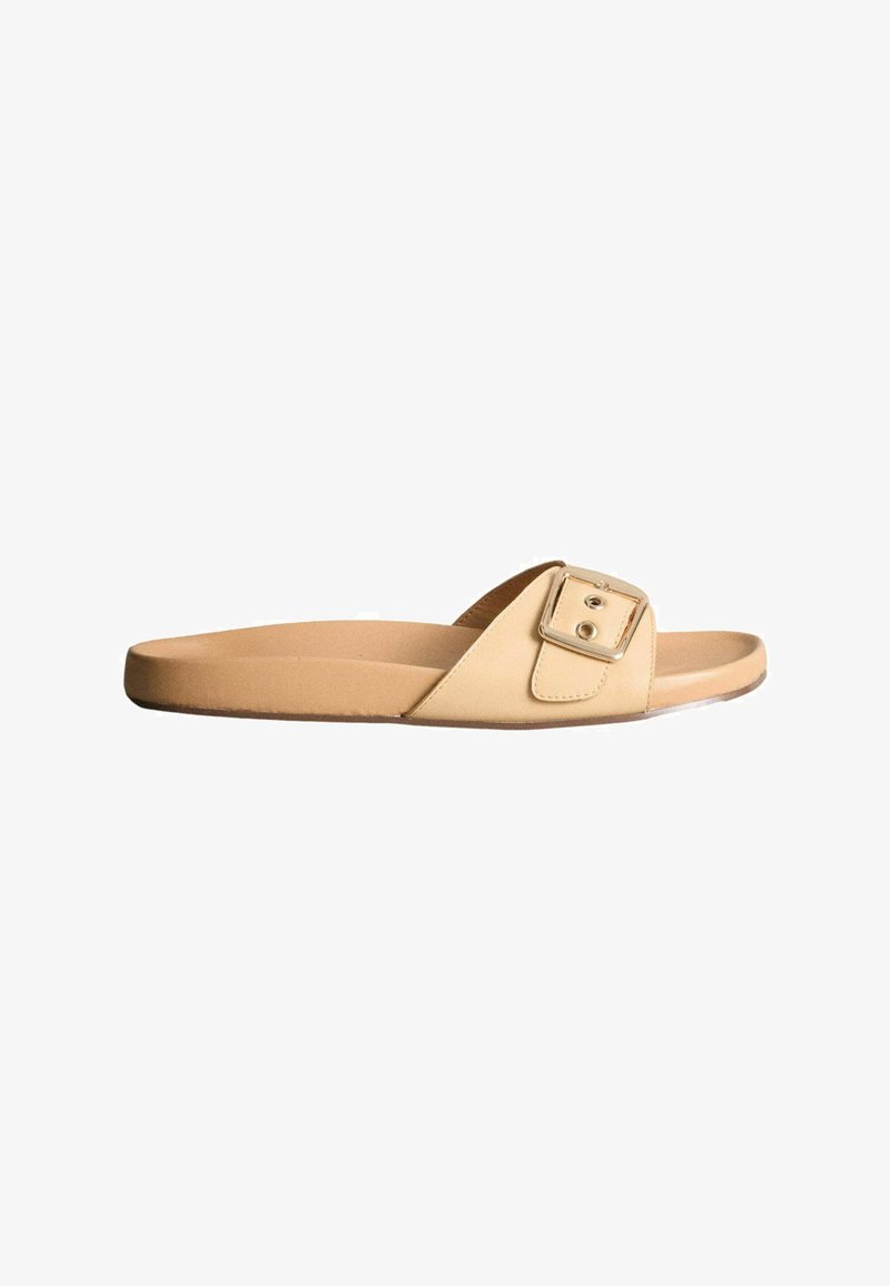 Sandale à glissière beige avec une semelle plate et une bride réglable ornée d'une grande boucle carrée sur fond blanc.