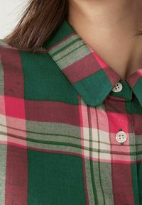 Chemise à carreaux verts et roses avec un col pointu, dotée de boutons blancs et d'une texture de tissu lisse.