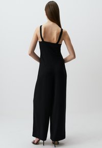 Zwarte jumpsuit met wijde benen, aansluitende bodice en dikke riemen. Glad stof met minimale naden, met een strakke, moderne uitstraling.