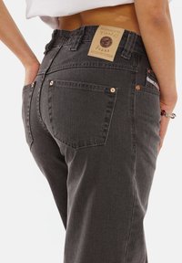 Gray denim jeans with a high waist, featuring copper rivets, a branded leather patch, and classic back pockets. Smooth texture.