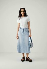 Λευκό βαμβακερό T-shirt με μικρές πράσινες εκτυπώσεις κακτοειδών, σε συνδυασμό με μια ανοιχτό μπλε τζιν μεγάλη φούστα, μαύρες λουριές σανδάλια και μια μικρή μπλε τσάντα.