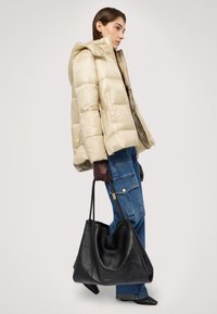 Béžová prošívaná bunda s kapucí, spárovaná s modrými cargo džíny a tmavými rukavicemi. Celkový vzhled doplňuje velká černá kožená taška.
