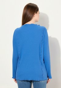Sininen pitkähihainen paita ribbikankaasta, jossa on aaltoileva reuna ja kontrastivär stitching saumoissa, sekä pyöreä kaula-aukko.