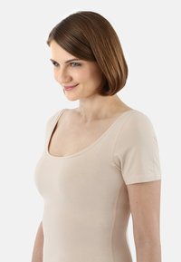 Nackter Kurzarm-Body mit weitem Rundhalsausschnitt, aus weichem, dehnbarem Stoff gefertigt. Verfügt über nahtlose Kanten für eine glatte Silhouette.