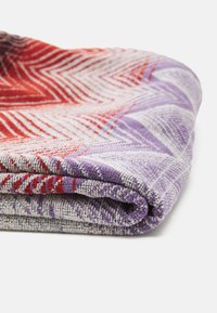 Manta texturizada en rojo, púrpura y gris con un patrón de Chevron, doblada para mostrar la suave trama y los colores vibrantes.