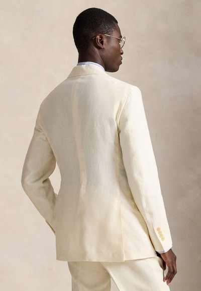 Kreminės spalvos lininis švarkas, pritaikytas figūrai, su vienu galiniu skeltuku, įpjautomis atlapomis ir keturių mygtukų detalėmis ant rankovių.