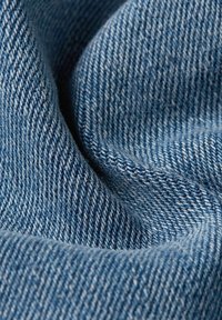 Nära bild av blå denimtyg som visar den vävda texturen och det diagonala twillmönstret med mjuka veck.