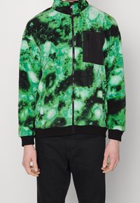 Giacca in pile con un motivo astratto verde e nero, chiusura con zip, collo alto e una tasca sul petto nera. Polsini e orlo neri a costine.