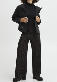 Černý vlněný kabát se zapínáním na cvoky, zkombinovaný s širokými hnědými kalhotami s tmavým zebrovým vzorem. Model nosí černý rolák.