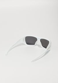 Óculos de sol brancos com lentes pretas, apresentando um design envolvente e hastes retas. Destaca-se a marcação dourada notável na lateral.
