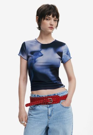 Fitted short-sleeve top in blue gradient, ribbed texture, round neckline. Paired with high-waisted light denim and a red studded belt.