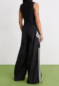Body atlético negro combinado con pantalones anchos negros que presentan franjas laterales blancas. Textura suave y cintura elástica para mayor comodidad.