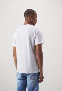 Witte katoenen t-shirt met een ronde hals, korte mouwen en een rechte pasvorm, gedragen met lichtblauwe spijkerbroek.