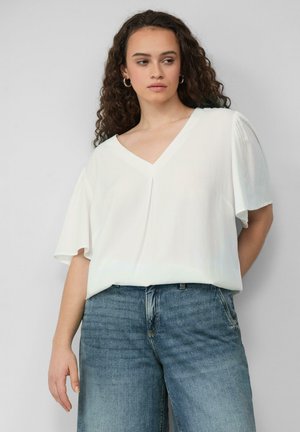 Weiße Bluse mit kurzen Ärmeln und V-Ausschnitt aus weichem, fließendem Stoff, kombiniert mit hellblauen, weiten Denim-Jeans.