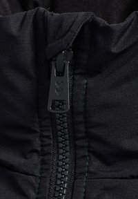 Close-up van een zwarte rits met een chevron-ontwerp op het trekkoord tegen een zwarte stofachtergrond.