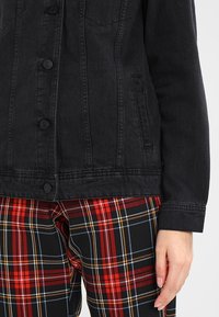 Black denim jacket with a buttoned front, chest pockets, and a classic collar, paired with red and black plaid pants featuring white accents.
